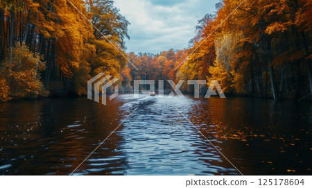 A canoe glides quietly along a river, bordered by vibrant autumn foliage under a moody sky, creating a peaceful outdoor experience. 125178604