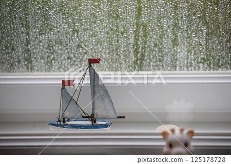 Toy Sailboat on Windowsill with Raindrops on Glass 125178728