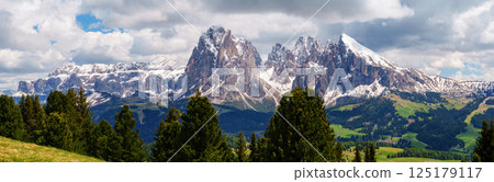 Majestic mountain range panorama with snowy peaks and lush greenery near Valley of Funes at Dolomites, Italy 125179117