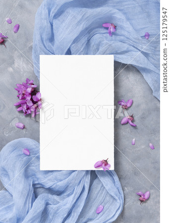 Vertical blank card on fabric near wild purple flowers top view on gray, spring wedding mockup 125179547