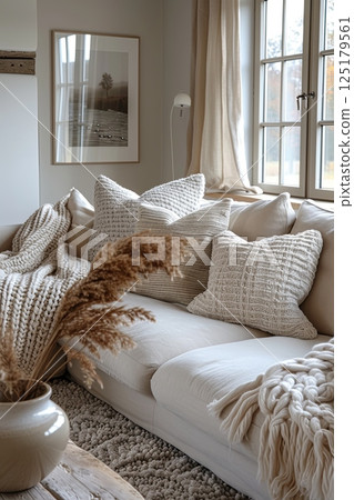 White couch with blanket draped over it and vase of dried grass on the floor 125179561