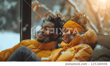 A couple bundled in yellow winter jackets relax by a window, enjoying the snowy view. 125180436