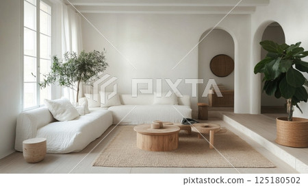 The sunlit living room features a spacious layout with a white sofa, wooden coffee tables, and greenery, creating a calm and inviting atmosphere that promotes relaxation and comfort. 125180502