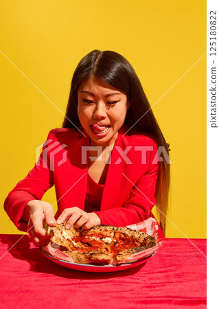 Young Asian woman expressing excitement to eat delicious pizza, taking slice from plate against bright studio background. Young Asian woman expressing excitement to eat delicious pizza, taking slice from plate against bright studio background. 125180822