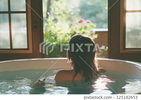 A woman is sitting in a bathtub with her hair wet A woman is sitting in a bathtub with her hair wet 125182653