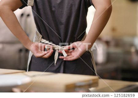Close up of a young chef tying apron before preparing a meal in a commercial kitchen setting. 125182659