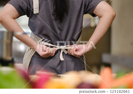 Close up of a young chef tying apron before preparing a meal in a commercial kitchen setting. 125182661