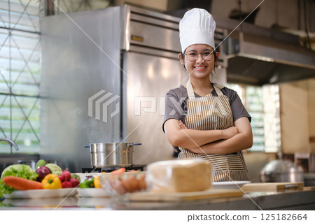 Portrait young teen girl cook student. Cooking class. Culinary classroom. Happy young woman students for cooking in cooking school. Portrait young teen girl cook student. Cooking class. Culinary classroom. Happy young woman students for cooking in cooking school. 125182664