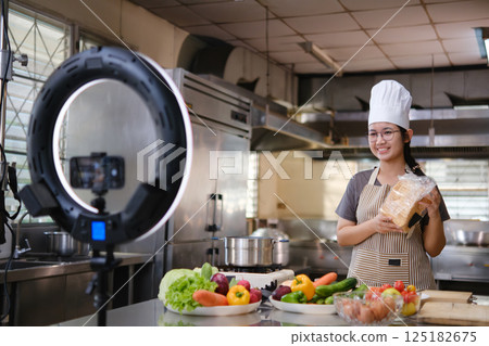 Food vlogger filming a cooking video in professional kitchen studio. 125182675