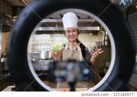 Food vlogger filming a cooking video in professional kitchen studio. Food vlogger filming a cooking video in professional kitchen studio. 125182677