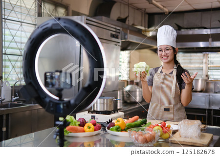 Food vlogger filming a cooking video in professional kitchen studio. 125182678