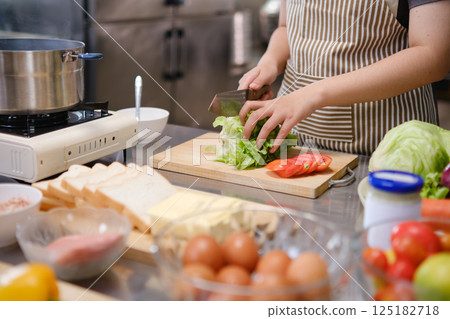 Young woman slicing vegetables in kitchen. 125182718