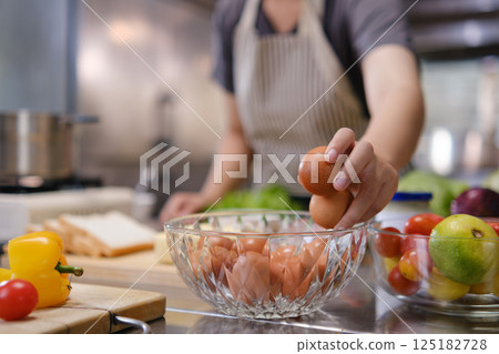 Chef picking fresh brown eggs from a glass bowl in a kitchen filled with colorful produce Chef picking fresh brown eggs from a glass bowl in a kitchen filled with colorful produce 125182728