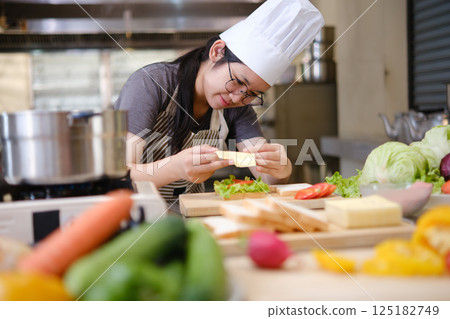 Focused chef carefully a gourmet sandwich in a professional kitchen with fresh ingredients in view 125182749