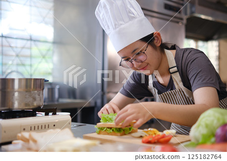 Focused chef carefully a gourmet sandwich in a professional kitchen with fresh ingredients in view 125182764