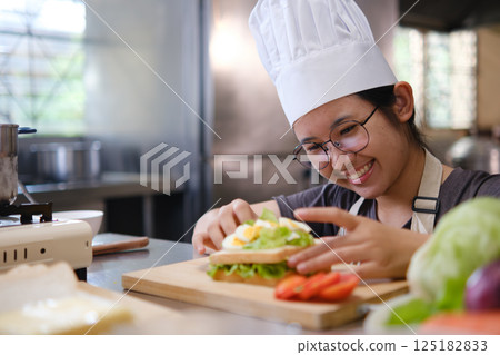Focused chef carefully a gourmet sandwich in a professional kitchen with fresh ingredients in view 125182833