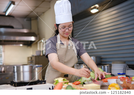 Chef adding ham slice to a fresh sandwich in a commercial kitchen. 125182840