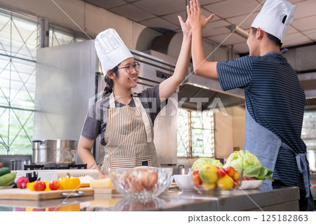Two smiling chefs giving a high five in a kitchen after a successful cooking session Two smiling chefs giving a high five in a kitchen after a successful cooking session 125182863