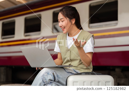 Traveling and Digital Connection. A young woman engages in video calling while waiting for her train. Traveling and Digital Connection. A young woman engages in video calling while waiting for her train. 125182982