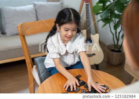 Family Bonding and Playtime. A young girl joyfully playing dominoes with her mother at home. Family Bonding and Playtime. A young girl joyfully playing dominoes with her mother at home. 125182984
