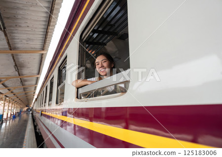Memorable Journeys and Happiness. A woman joyfully peeks out of a train window, capturing a moment of travel excitement. Memorable Journeys and Happiness. A woman joyfully peeks out of a train window, capturing a moment of travel excitement. 125183006