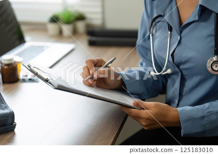 Documentation and Patient Care. A nurse records patient information during a medical consultation. 125183010