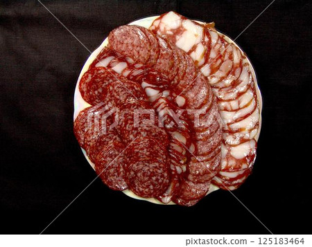 Slices of sausage and lard on a plate over solid background Slices of sausage and lard on a plate over solid background 125183464