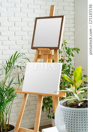 Empty easels stand ready for artistic creation in a bright indoor space surrounded by greenery 125183536