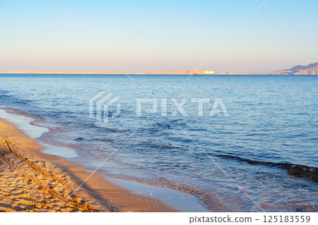 Relaxing sunset view over calm ocean waves and sandy beach at coastal location Relaxing sunset view over calm ocean waves and sandy beach at coastal location 125183559