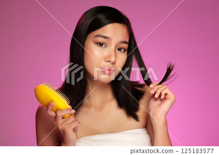 Young woman with long hair styling in front of a colored background during a beauty routine Young woman with long hair styling in front of a colored background during a beauty routine 125183577