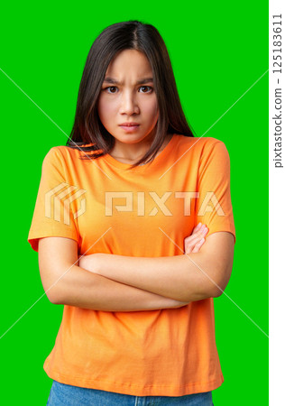 Young woman expressing frustration while standing against a bright green background in casual attire Young woman expressing frustration while standing against a bright green background in casual attire 125183611