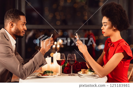 Modern Relationship. Serious African American Couple Using Mobile Phones Having Romantic Date In Restaurant. Modern Relationship. Serious African American Couple Using Mobile Phones Having Romantic Date In Restaurant. 125183981