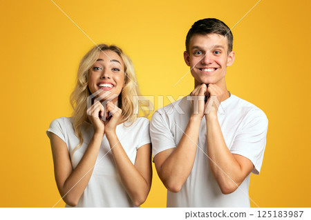 Young smiling guy and girl pleading for something together, clasping hands over yellow background, closeup Young smiling guy and girl pleading for something together, clasping hands over yellow background, closeup 125183987