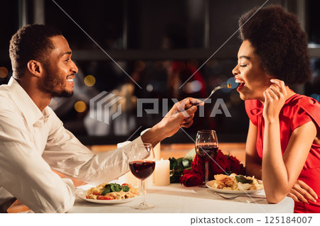 Romantic Date Concept. African American Man Feeding Girlfriend During Dinner Celebrating Anniversary In Restaurant Romantic Date Concept. African American Man Feeding Girlfriend During Dinner Celebrating Anniversary In Restaurant 125184007