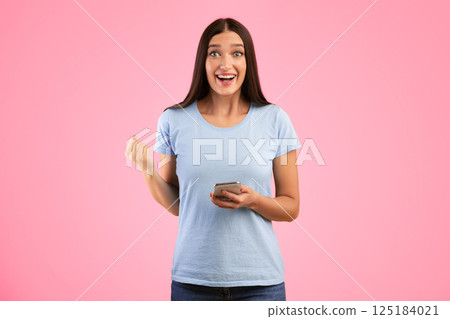 Yes. Portrait of happy surprised young woman using smartphone making winner gesture isolated over yellow studio wall background. Excited lady celebrating win, shaking clenched fist, looking at camera Yes. Portrait of happy surprised young woman using smartphone making winner gesture isolated over yellow studio wall background. Excited lady celebrating win, shaking clenched fist, looking at camera 125184021