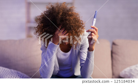 Depressed girl holding pregnancy test covering face with hand, sitting on couch, free space Depressed girl holding pregnancy test covering face with hand, sitting on couch, free space 125184034