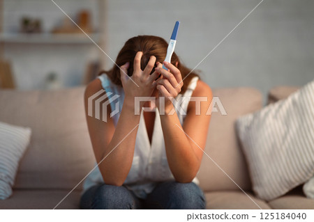 Unrecognizable Depressed Girl Holding Pregnancy Test Covering Face With Hands Sitting On Couch Indoor. Selective Focus 125184040