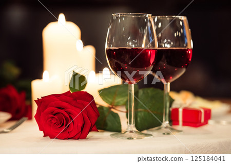 Valentine's Day Background. Two Red Wine Glasses And Rose Lying On Restaurant Table Served For Romantic Date. Selective Focus Valentine's Day Background. Two Red Wine Glasses And Rose Lying On Restaurant Table Served For Romantic Date. Selective Focus 125184041