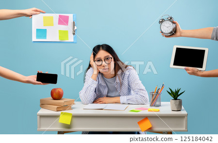 Deadline and multitask concept. Tired asian lady stressed by a lot of work, sitting at the desk over blue background and looking at camera. Hands with tablet, watch, tasks and smartphone Deadline and multitask concept. Tired asian lady stressed by a lot of work, sitting at the desk over blue background and looking at camera. Hands with tablet, watch, tasks and smartphone 125184042