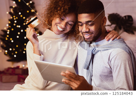 Christmas holiday. African-american couple choosing gifts on tablet, using credit card 125184043