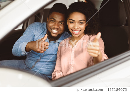 New Auto. Joyful African Couple Gesturing Thumbs Up Sitting In Car Buying Vehicle In Dealership Showroom. Selective Focus New Auto. Joyful African Couple Gesturing Thumbs Up Sitting In Car Buying Vehicle In Dealership Showroom. Selective Focus 125184073