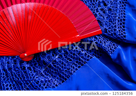 Red fan on blue lace fabric. Vibrant contrast of color and texture Red fan on blue lace fabric. Vibrant contrast of color and texture 125184356
