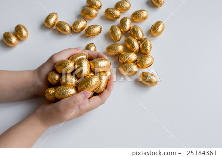 Childs hands holding golden chocolate Easter eggs on white background Childs hands holding golden chocolate Easter eggs on white background 125184361