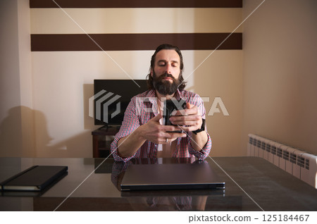 Young Man Using Smartphone at Desk in a Modern Home Office 125184467