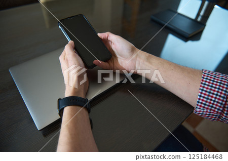 Businessman Using Smartphone on Desk With Laptop in Modern Workspace Businessman Using Smartphone on Desk With Laptop in Modern Workspace 125184468