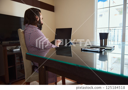 Focused Professional Working on Laptop at a Sunlit Home Office Desk 125184518