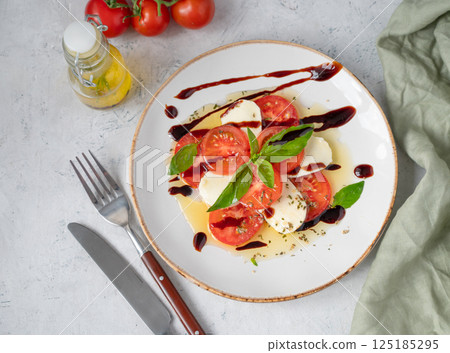 Caprese salad with sliced tomatoes, mozzarella and basil on a plate on a light background Caprese salad with sliced tomatoes, mozzarella and basil on a plate on a light background 125185295