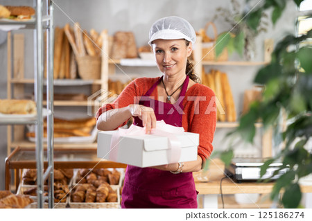 Woman entrepreneur owner of bakery holds out paper bag with pastries in hand Woman entrepreneur owner of bakery holds out paper bag with pastries in hand 125186274