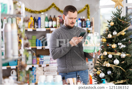 Middle-aged man scanning QR-code on gift basket in store during Christmas 125186352
