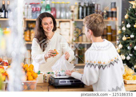 Woman sells sweets to teen boy, puts them on scale and weighs sweets, New Year Eve 125186353